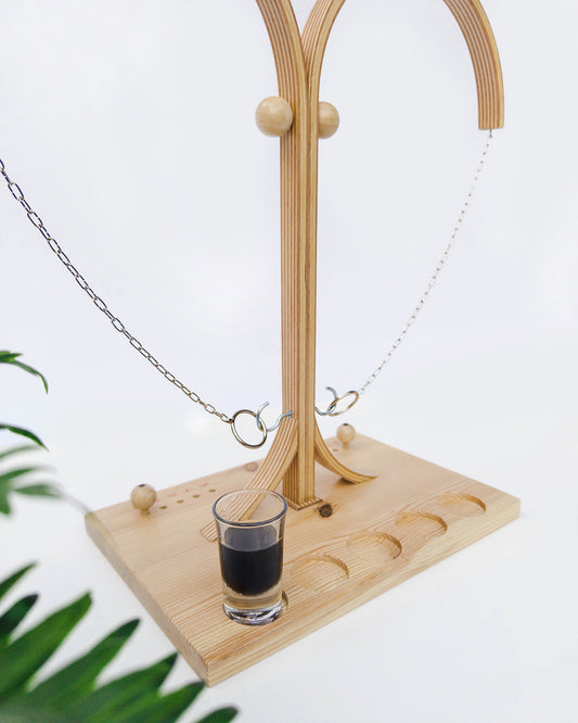 Lesena igra metanje obroca na kavelj, estetska oblika, ring hoo, hook and ring. Podbrobno spodnji del. Levo je na prvem mestu postavljen poln kozarec z žgano pijačo.