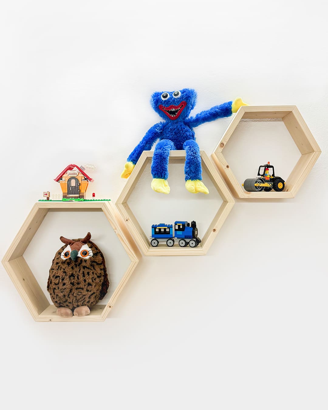 Lesene hexagonalne police z različnimi igračami, kot so plišasti medvedek, Lego hiša, traktor in vlak, ki so postavljene v kreativnem razporedu