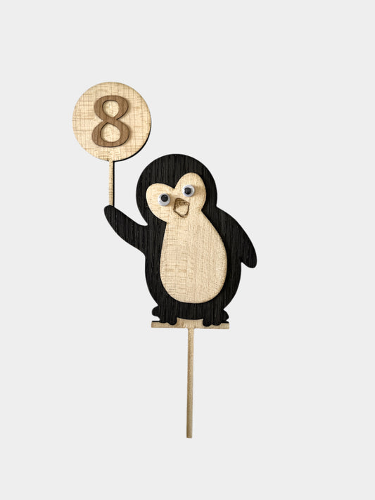 Lesena figura v obliki Pingvina, ki v svoji desni roki drži balon na katerem je številka 8. Figura je iz črnega furnirja in svetlo rjavega. Pingvin topper stoji na palici.