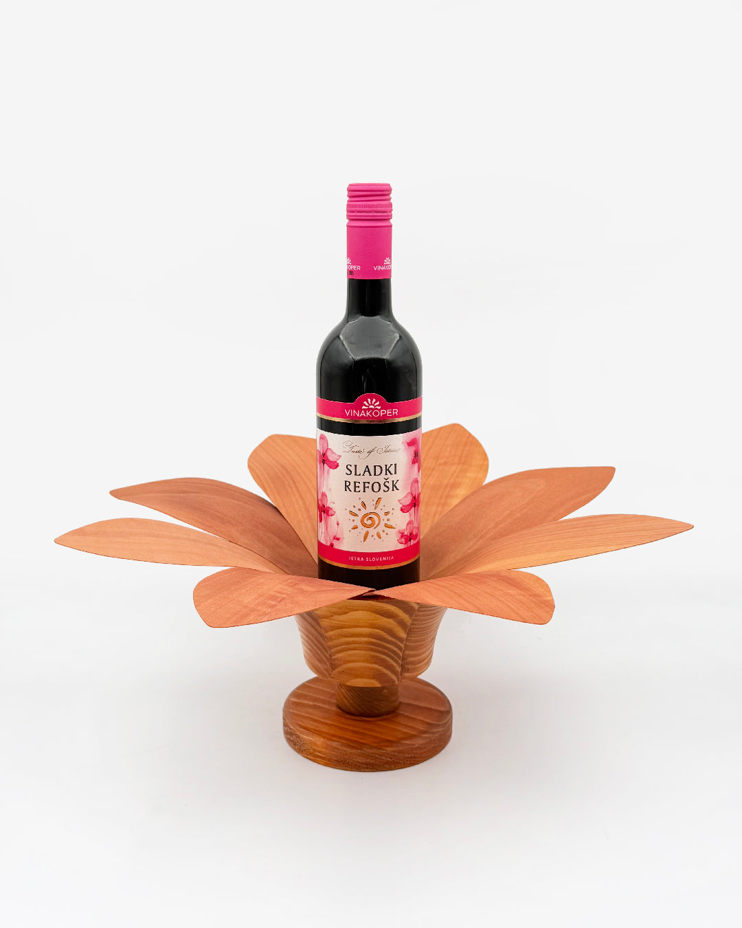 Lesena roža za vino s podstavkom. V sredico je postavljena steklenica sladkega refoška. Lahko je tudi kakršnokoli drugo vino. Cvetlica, roža je temno rjave barve.
