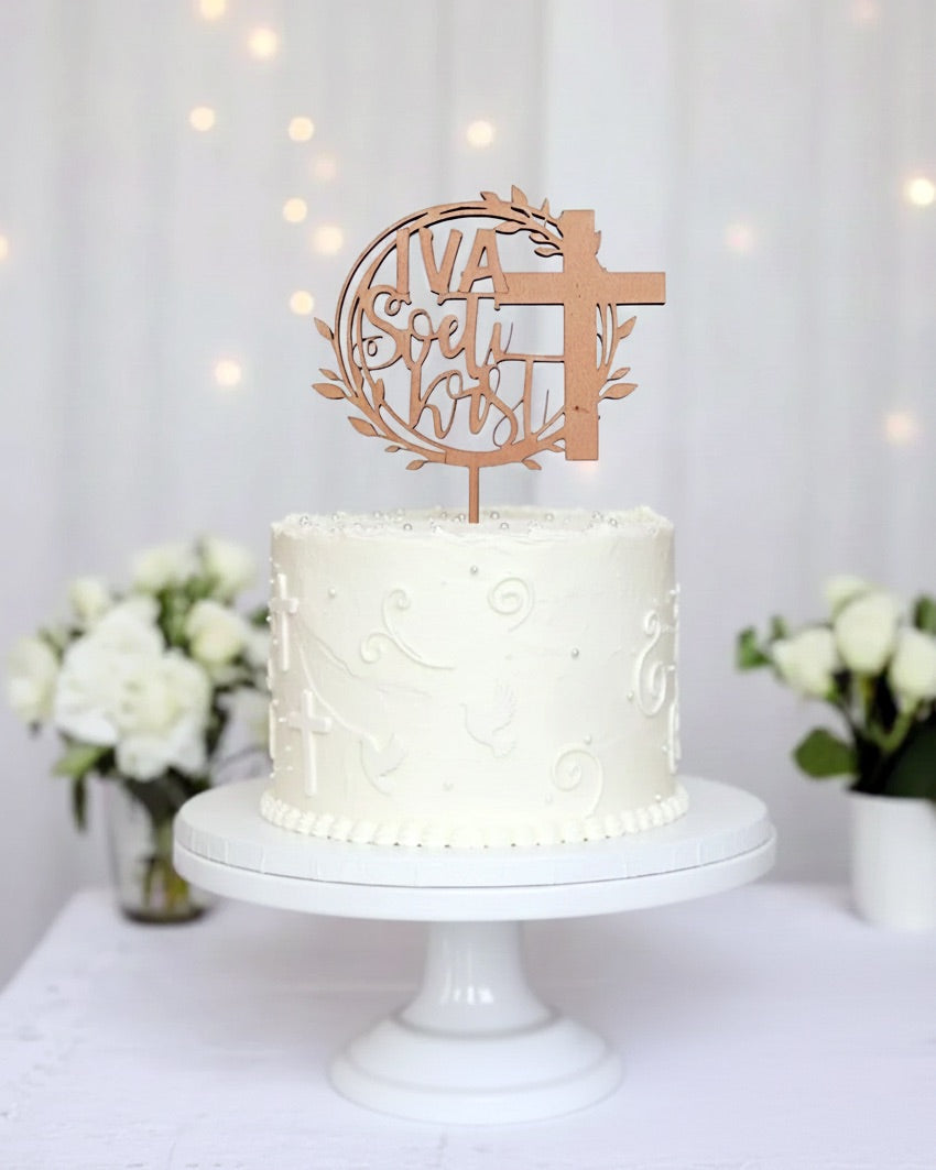 Personaliziran topper ali napis za torto  sveti krst. Toper je na sredini bele visoke torte. Je iz temnega furnirja. Na toperju je desno velik križ, levo zgoraj piše IVA, pod tem pa sveti krst.