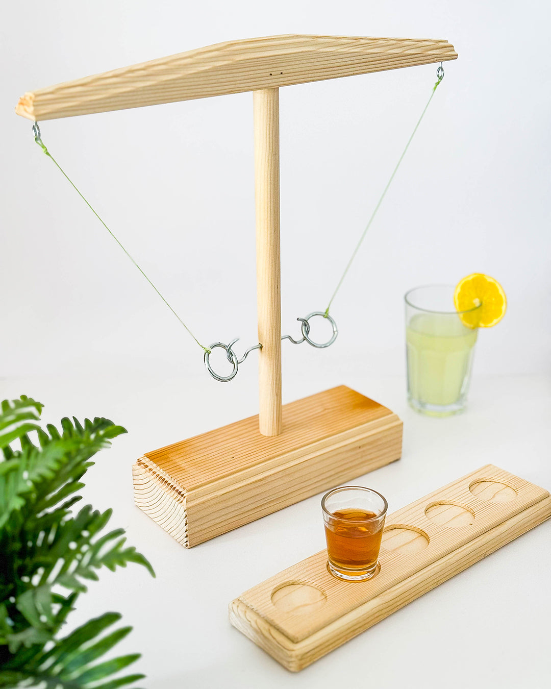 Zabavna igra met obroča na kavelj, hook and ring, ring hook, na sliki je od daleč poslikano stojalo s kavlji in obroči, zraven je dodana plošča za kozarec za žganje, aperitiv. Desno v sredini je še v kozarcu limonada za okras, levo spodaj pa zelena roža. Ring hook igra ali hook and ring.